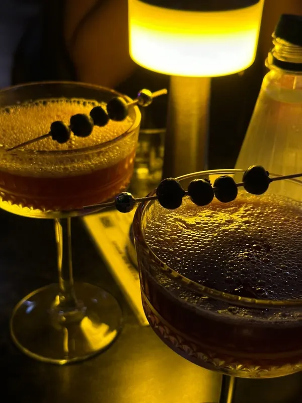 Two dark cocktails with skewered berries under a lamp
