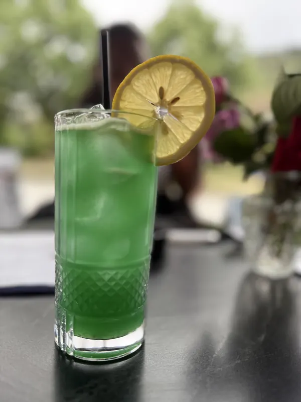A green long drink with a lemon wheel, outdoors by day