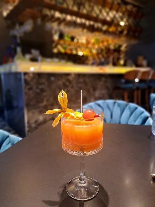 An orange cocktail with a physalis on a dark table