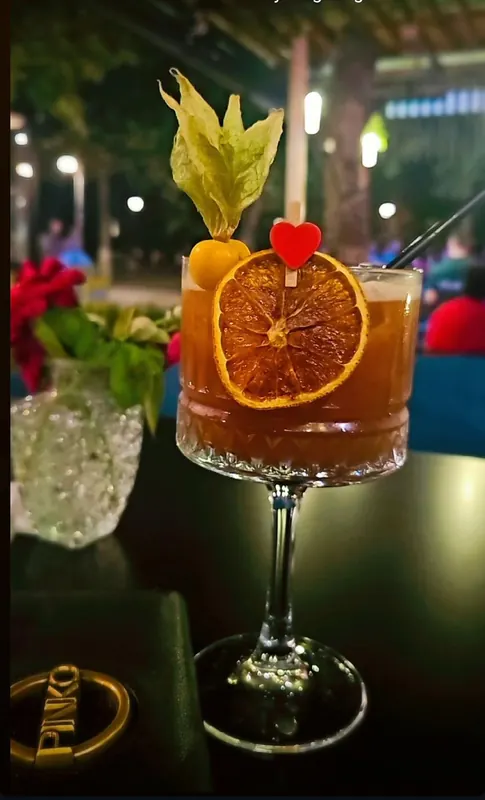 A cocktail in a coupe glass, garnished with a physalis and a dried orange wheel